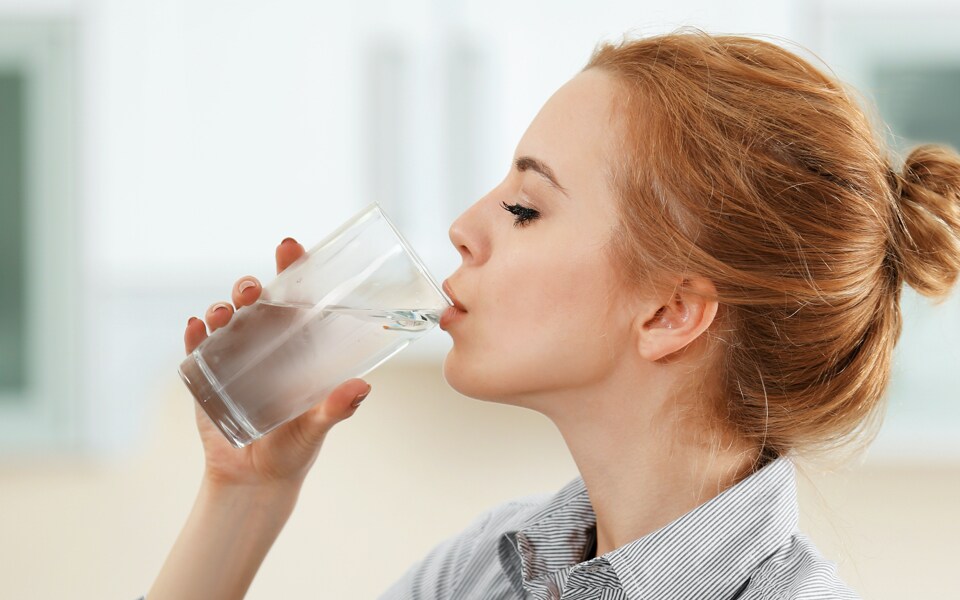 Frau mit Kinderwunsch trinkt Wasser in der Küche