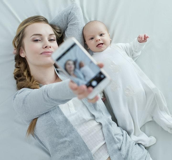 Mama liegt mit dem Baby und macht ein Selfie